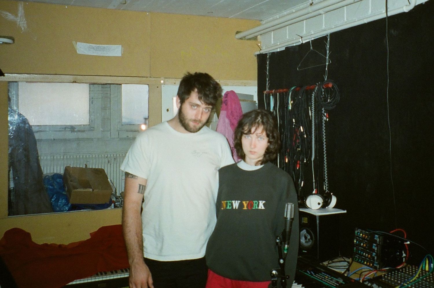 Das Bild zeigt die DJs mit Namen pretty lovely. Die beiden Personen stehen in einem kleinen Raum mit Mischpult, Kopfhörern und Keyboard. Sie tragen lockere Kleidung und blicken gerade in die Kamera.
