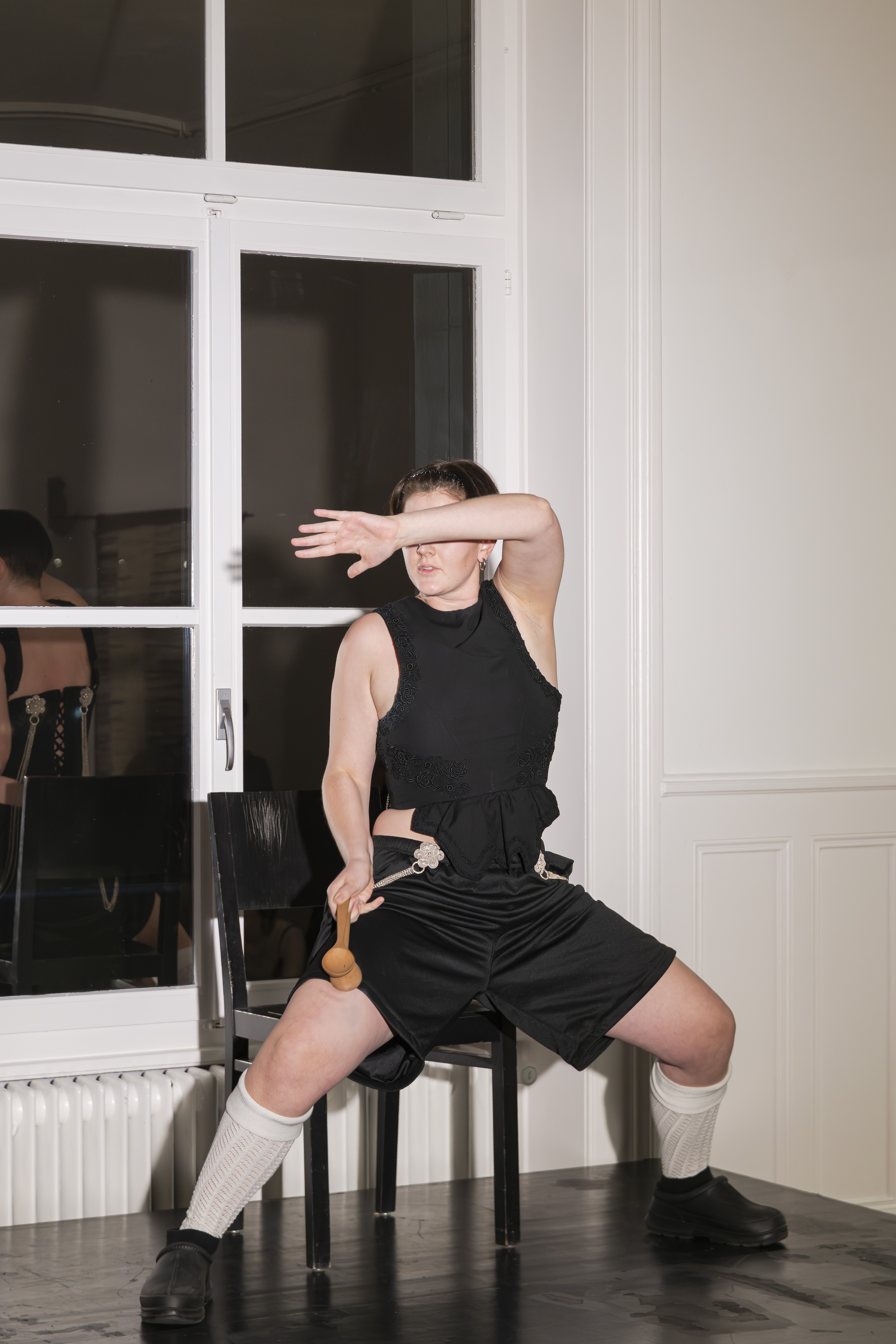 Eine Person sitzt auf einem schwarzen Stuhl. Sie hält zwei Löffel in der Hand und schlägt damit auf die Oberschenkel. Ein Unterarm bedeckt die Augen.