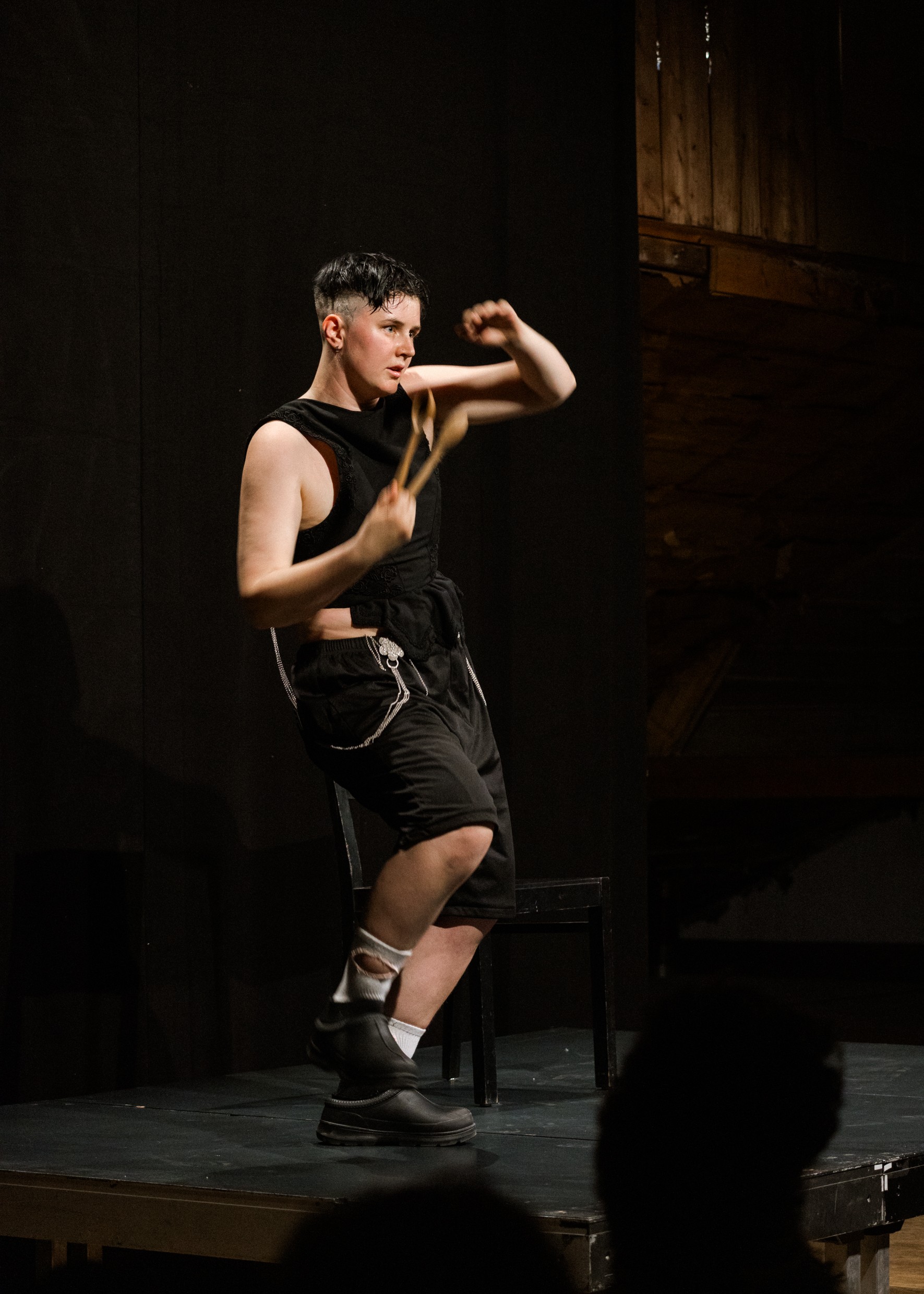 Eine Person ist schwarz gekleidet und hält in der rechten Hand zwei Löffel. Sie ist in Bewegung.