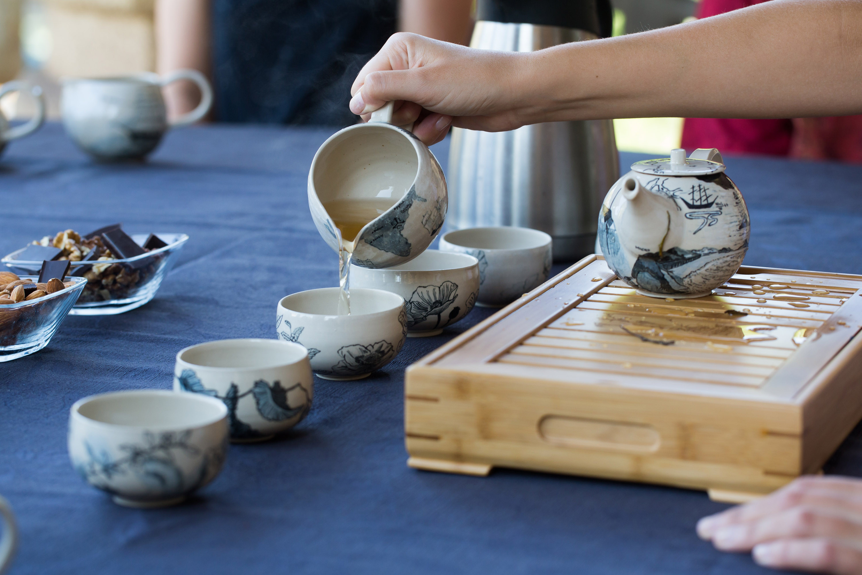 Man sieht weisses Keramikgeschirr mit blauer Malerei. Eine Hand giesst gerade Tee von einer kleinen Kanne in eine Tasse.