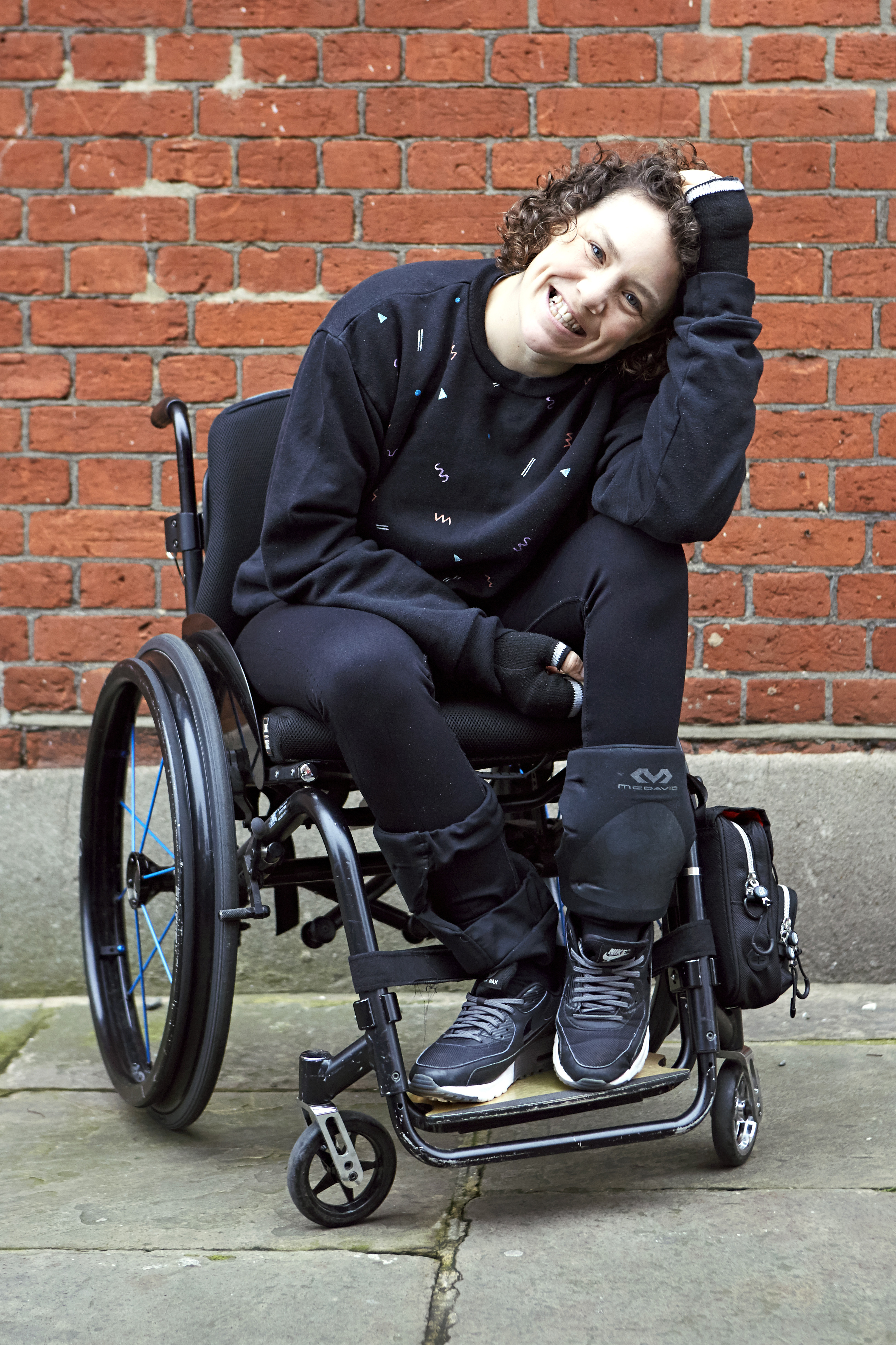 Die Künstlerin Jess Thom im Rollstuhl vor einer Backsteinwand