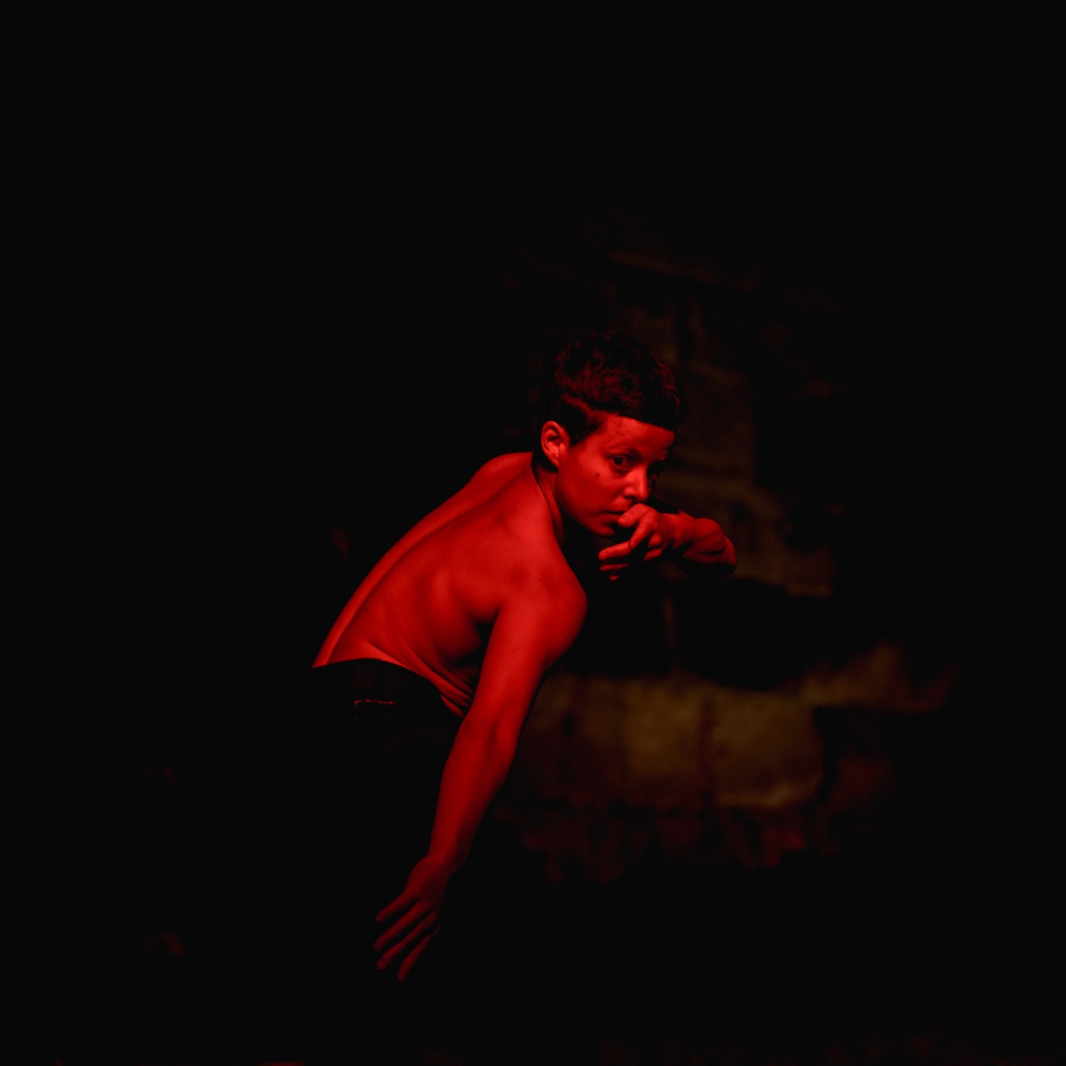 Catol Teixeira tanzt mit nacktem Oberkörper und schaut Richtung Kamera. Der ganze Raum ist in rotes Licht getaucht.