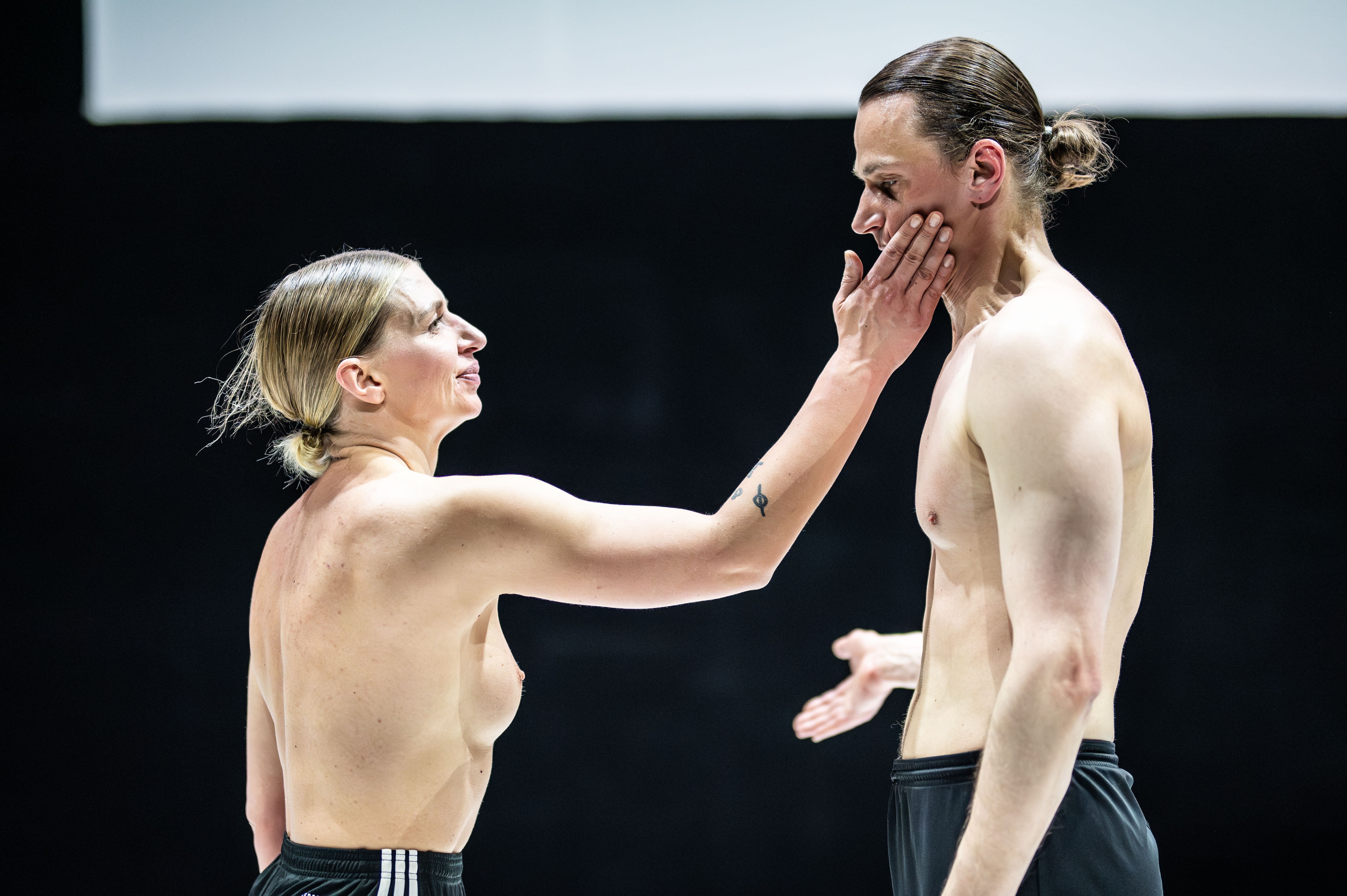 Eine Performerin und ein Performer stehen sich gegenüber. Die Performerin gibt dem Performer eine Ohrfeige. Beide tragen nur Hosen und sind oberkörperfrei.