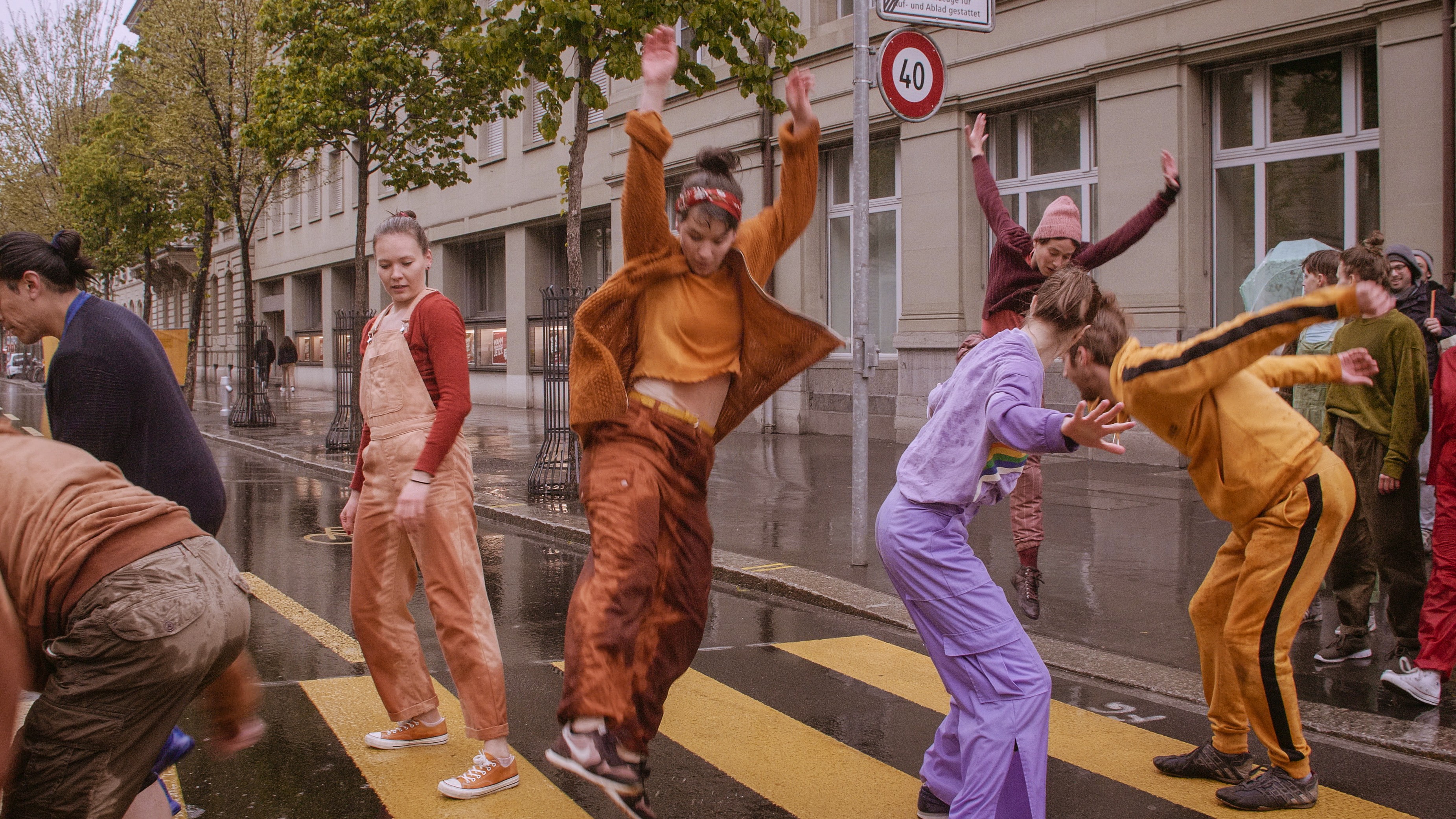 Eine Gruppe von Menschen in bunten Kostümen bewegen sich tanzend über einen Fussgängerstreifen.